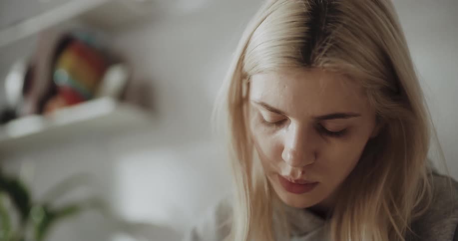 Young blonde woman sitting on the bed at home studying
