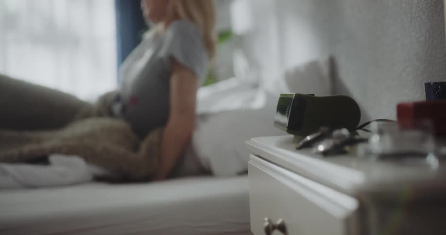 A young woman awakened by an alarm clock stops the alarm before stretching and climbing out of bed