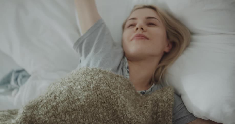 A sleeping woman awakens and stretches before climbing out of bed
