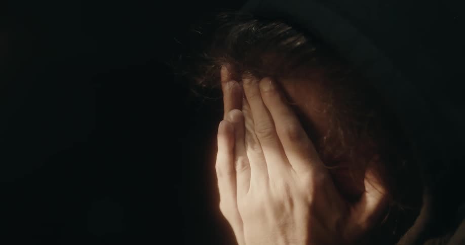 A view of a man sitting in a room with his head in his hands
