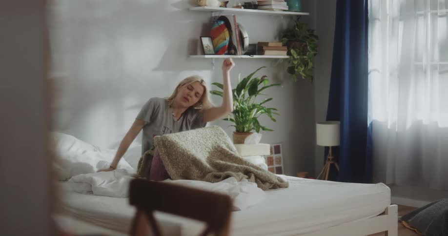 A young woman is awakened by an alarm clock and begins to stretch before preparing to get out of bed