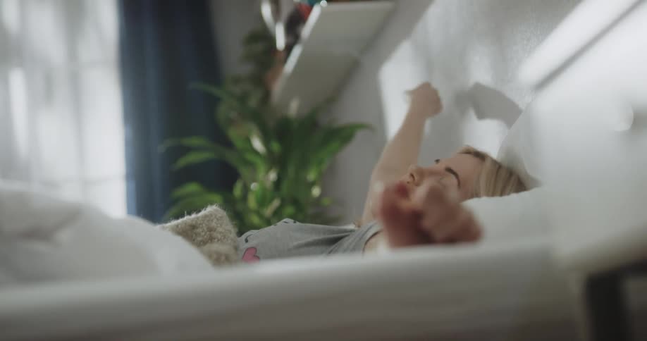 A sleeping young woman wakes up and stretches before climbing out of bed