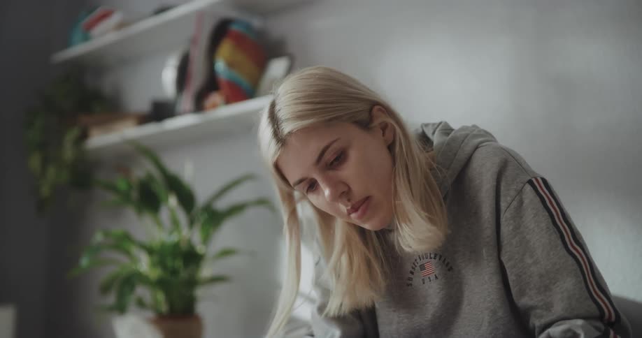 Young blonde woman sitting on the bed at home studying