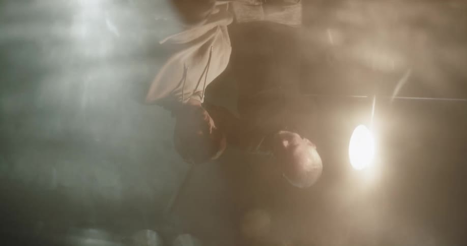 The reflection of a military man approaching a hooded prisoner and removing the hood for interrogation