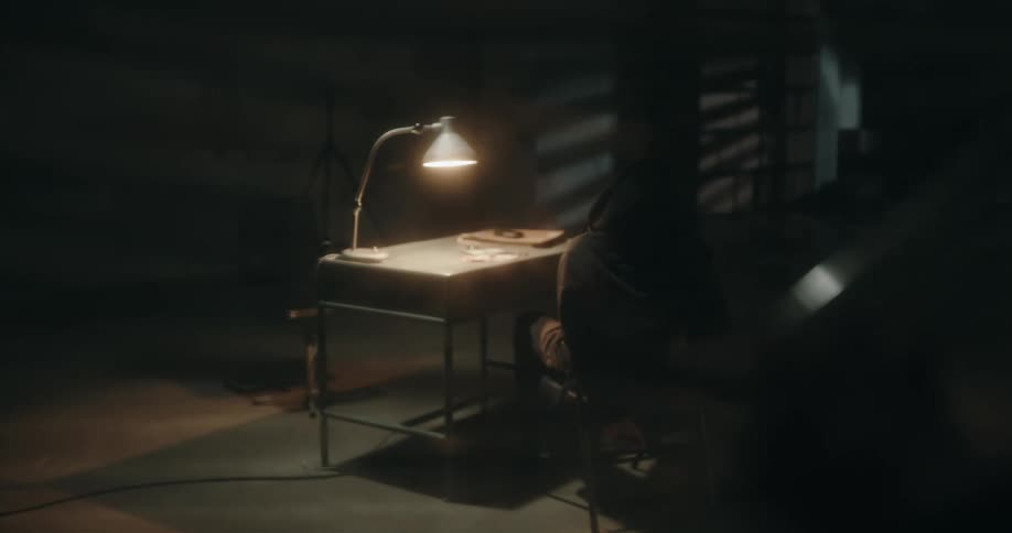 Person looks through blinds to check on individual sitting at table in interrogation room