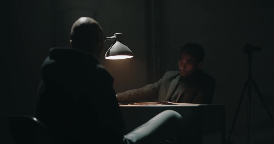 Detective questioning a suspect inside a dimly lit interrogation room