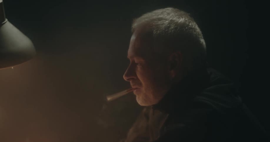 Detective lights a cigarette before showing pictures to a suspect sitting inside an interrogation room