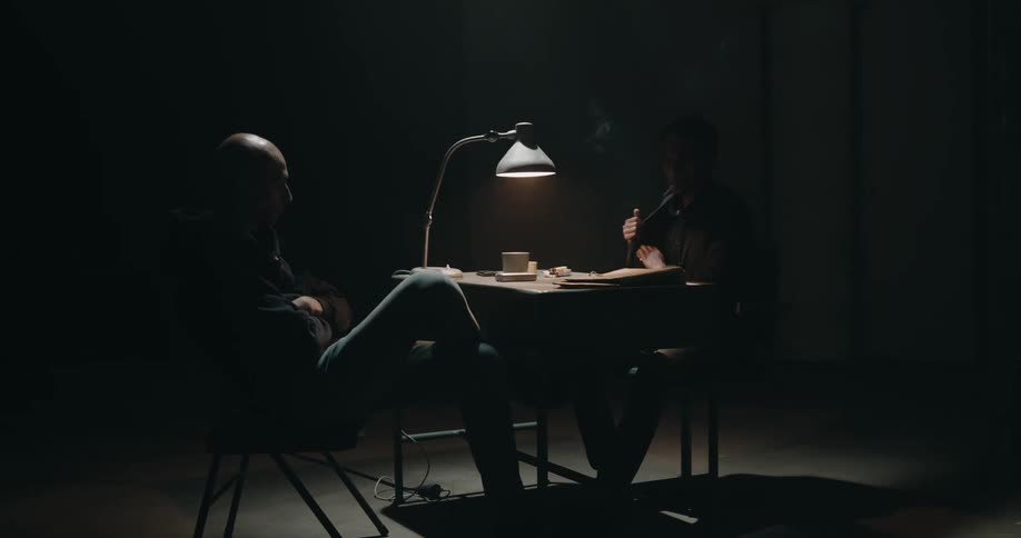 A detective interrogates a suspect in a dim room