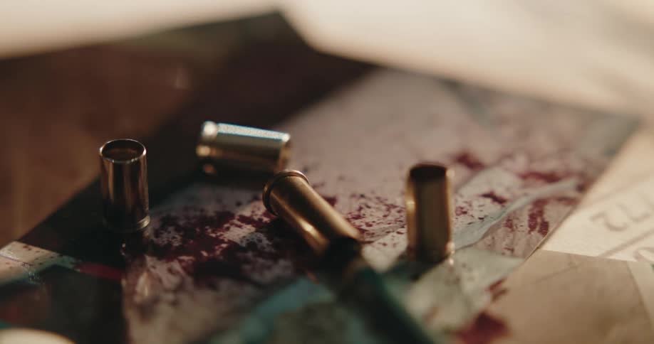 Bullet casings resting over a photograph covered in blood over a desk