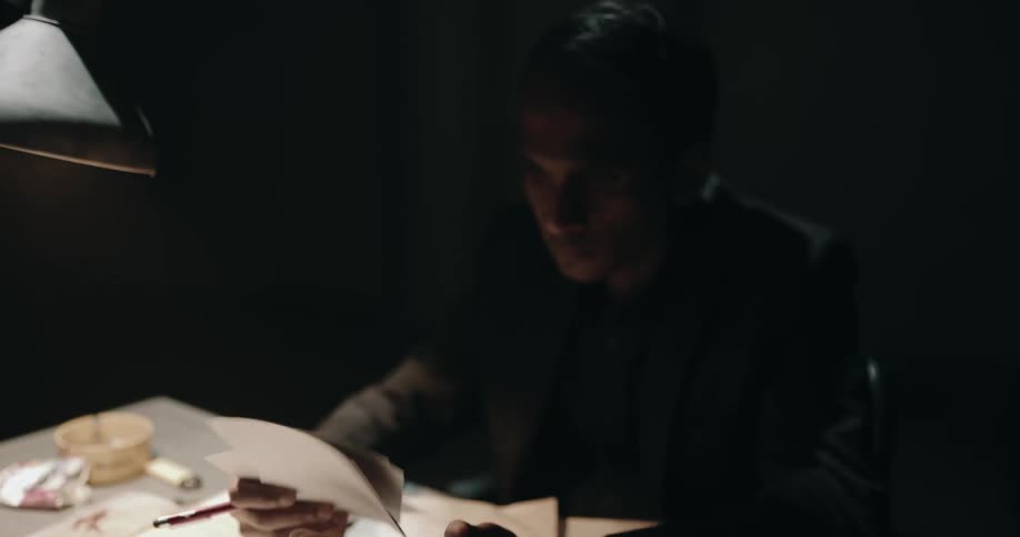 Detective checking files over a desk inside an interrogation room looks at the camera