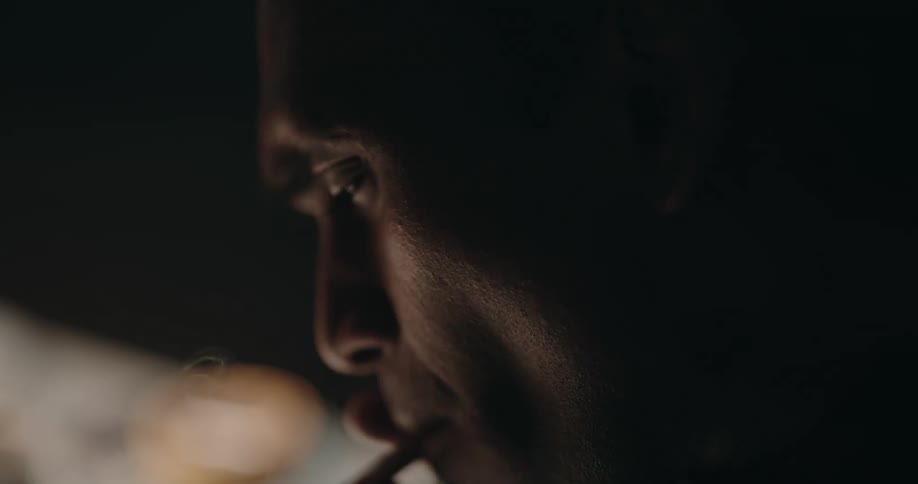 A man is smoking a cigarette and dips it into the ashtray as he sits at a table