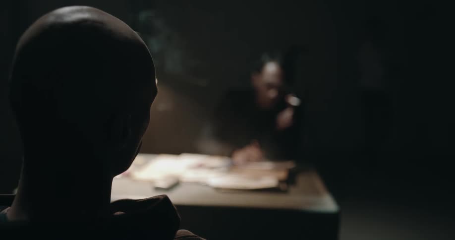 A man with a shaved head pulls his hood down sitting across from a military man