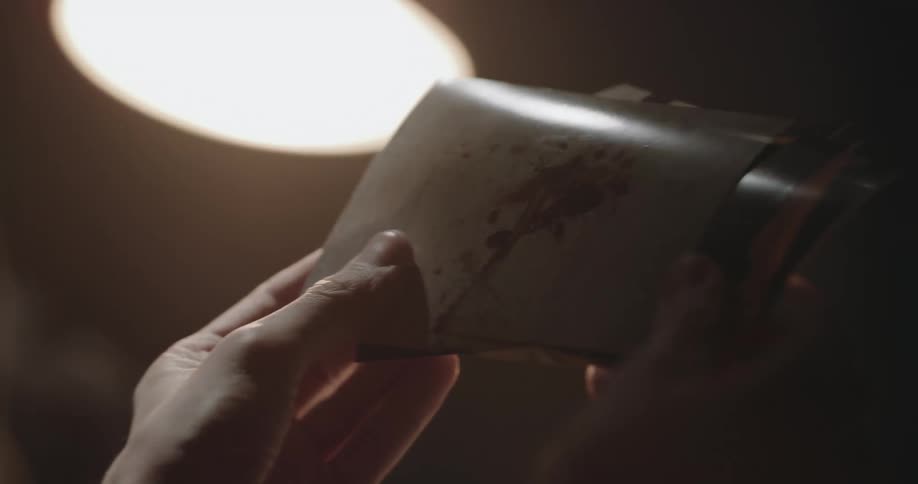 Suspect sitting on an interrogation room looks at photographs in front of a detective