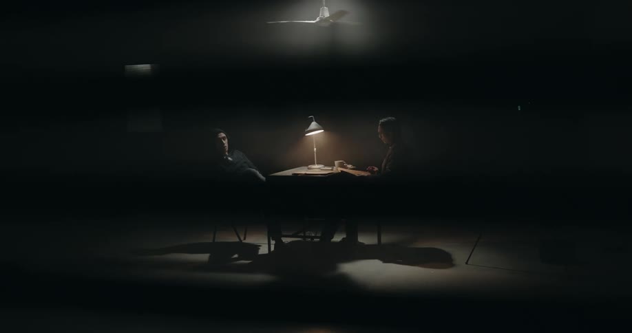 Policeman smokes while interrogating suspect in dark room