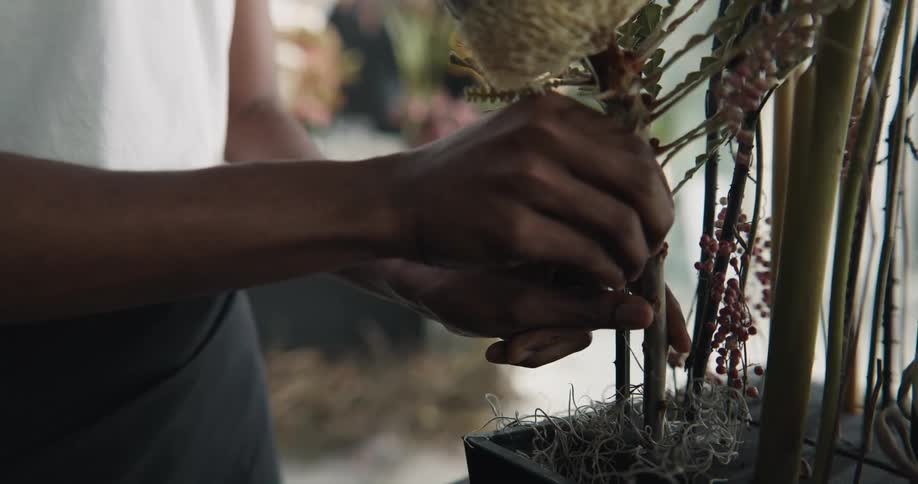 A woman trims a stem and places a thick flowering branch into an arrangement