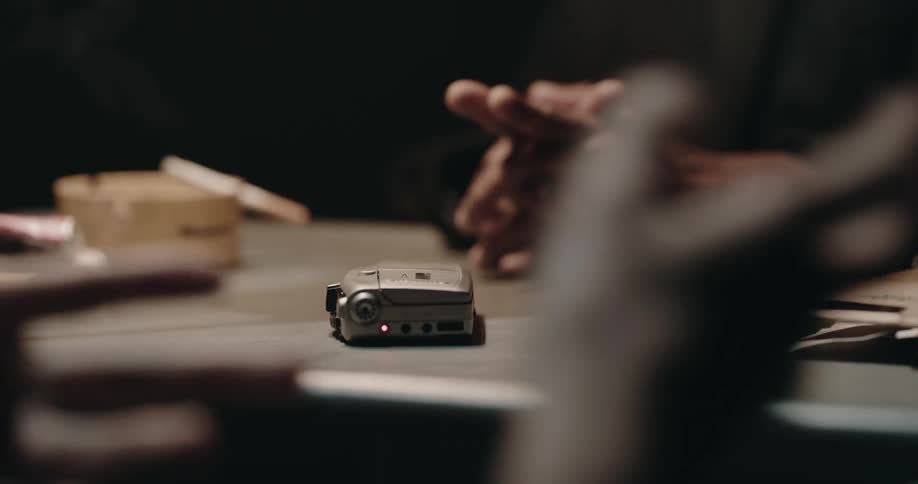 Suspect talks to a detective inside a dimly lit interrogation room in front of a tape recorder