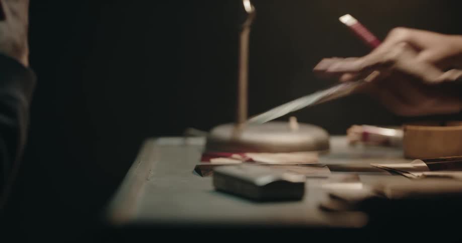 A man sitting at a desk opens a folder and puts photos in front of a man across from him and points at them