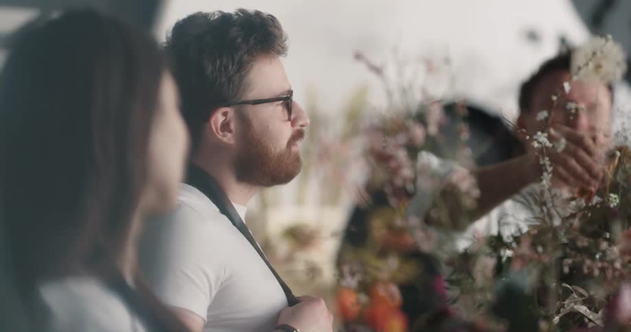 Boss of a flower shop teaches employees how o assemble a flower bouquet