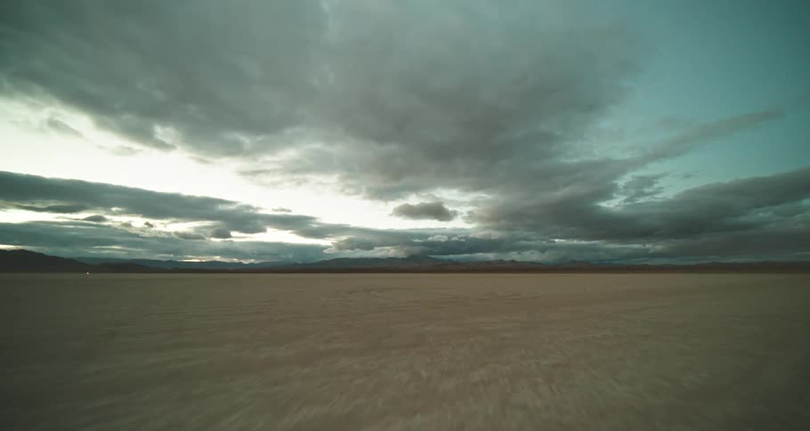 A dim light shines in the wide open desert with mountains on the horizon under a cloudy sky