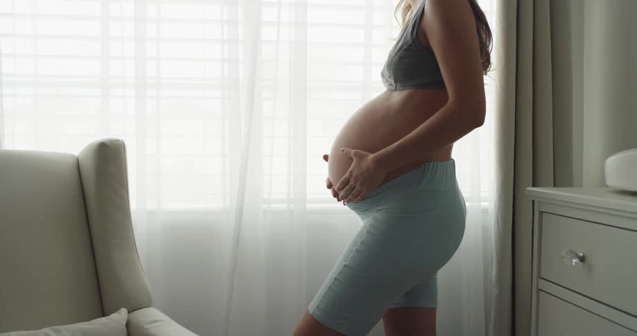 Pregnant woman is standing up as she rubs her belly