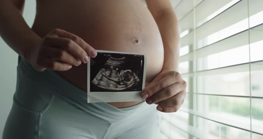 Pregnant women is standing by the window