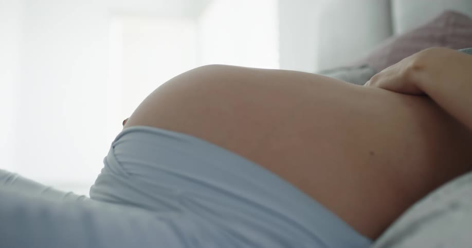 A pregnant woman strokes her stomach while resting in bed