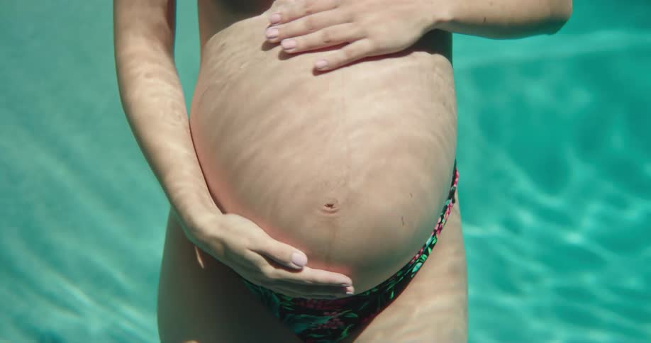 A pregnant woman rubs her stomach underwater
