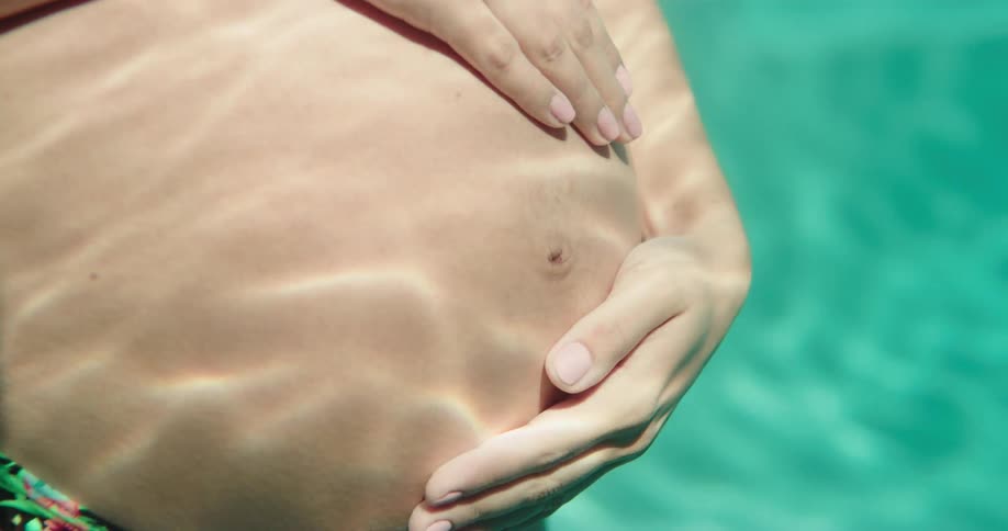 Pregnant woman with bikini touches her belly in the swimming pool