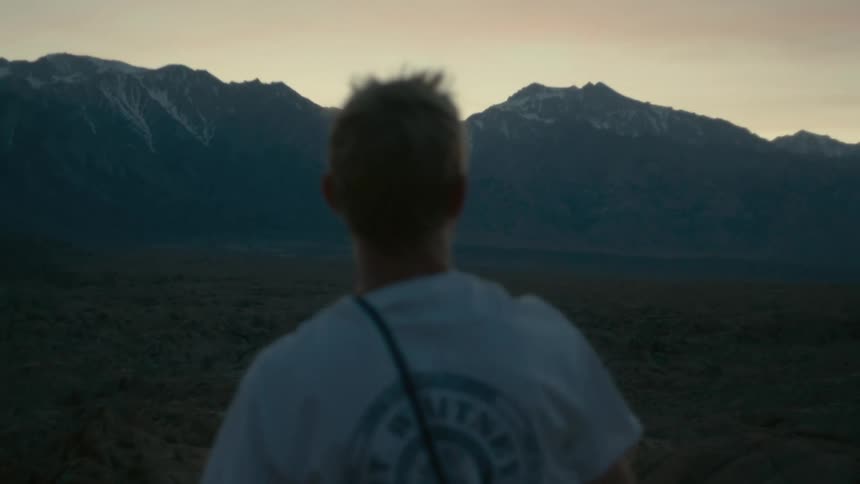 A man standing in a grassland points out at the distance mountains