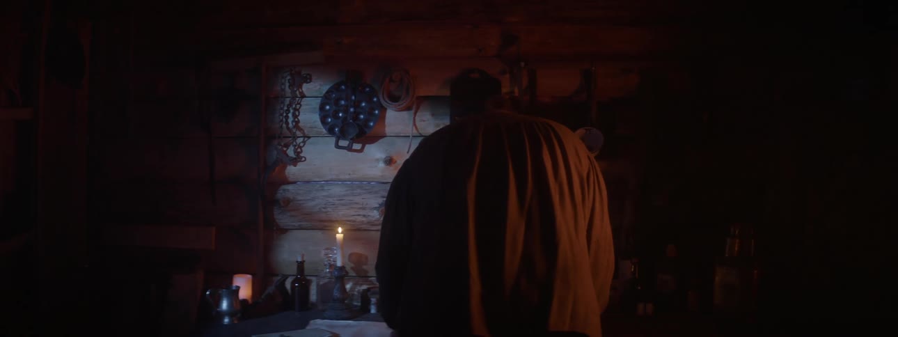 A man walks up to a table in a room poorly lit by candles