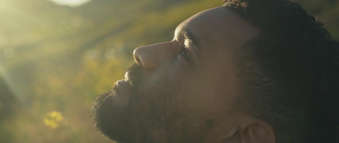 A man looks up at the sky while sitting in field during the day