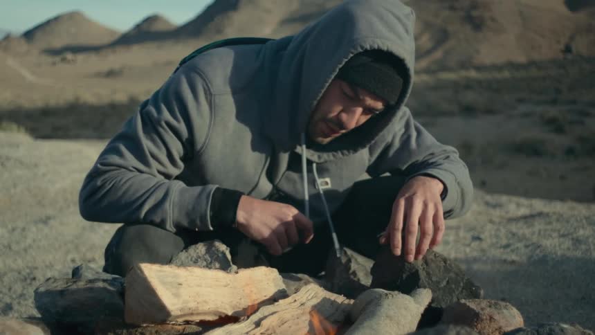 A man carefully watches a campfire in the badlands during the day