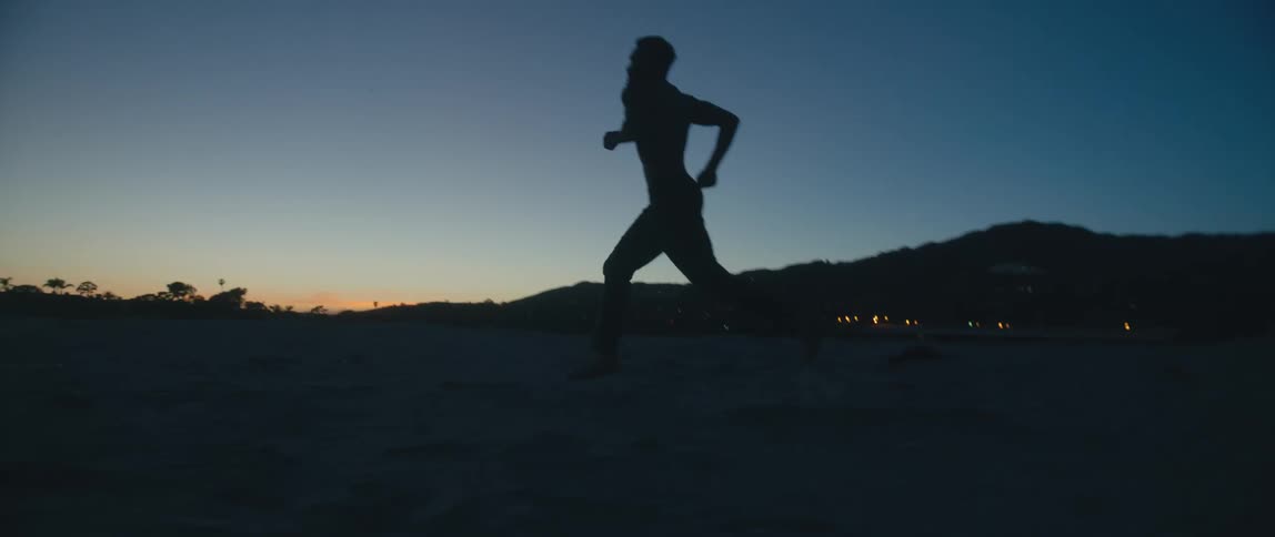 Man silhouetted against red tinted horizon with town lights in background