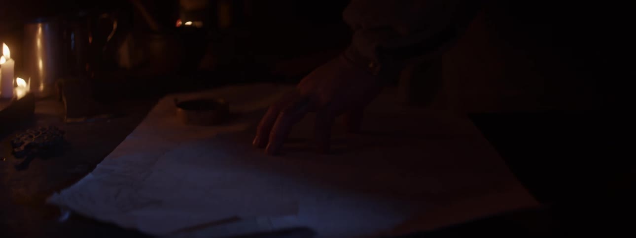 A man standing at a table reading a map using a compass and candle light