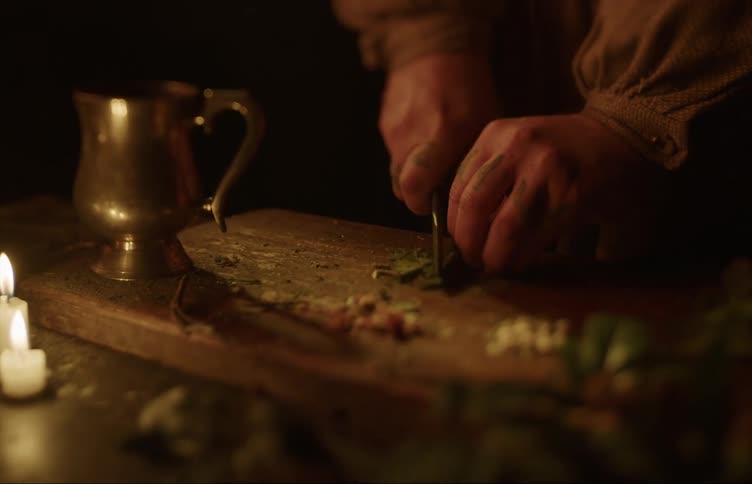 A person chops herbs by candlelight