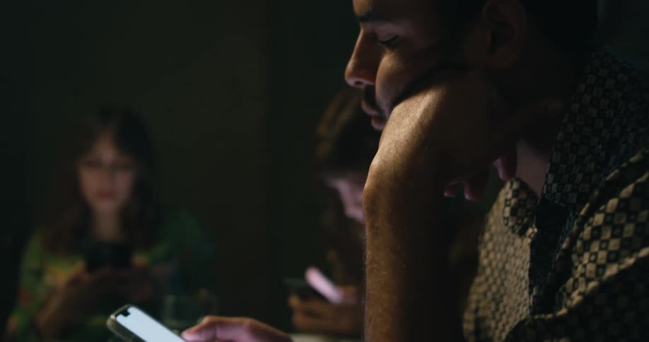 A man uses his smartphone while sitting at a dining table with other people focusing only on their phones