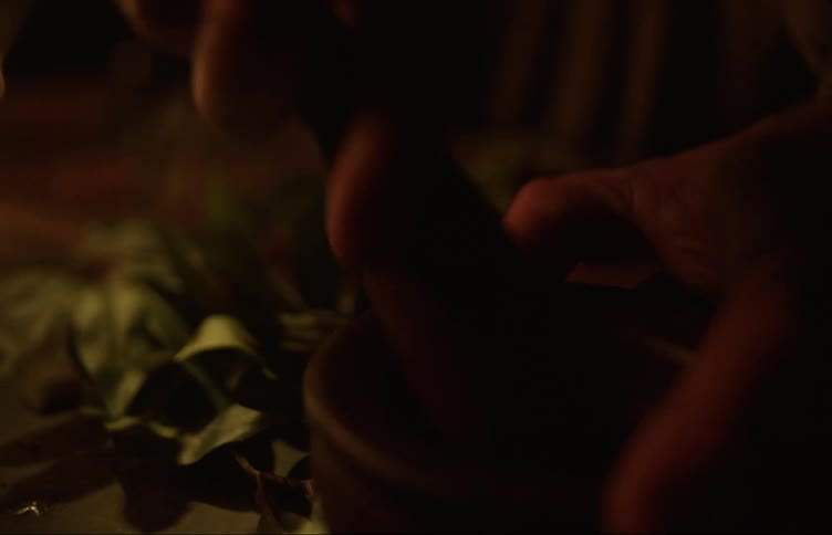 A cook mashing herbs inside a pestle and mortar on a dimly lit kitchen