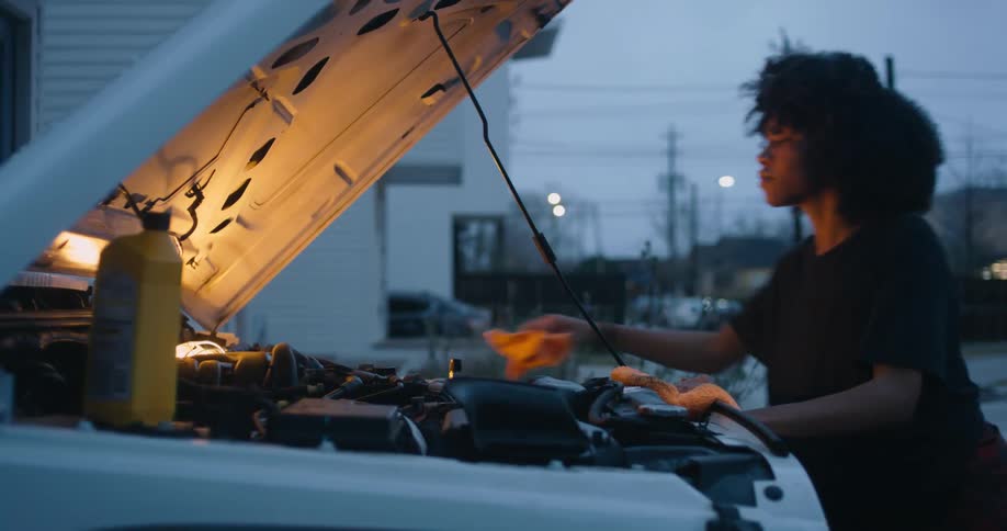 A woman is working on a car outdoors at night