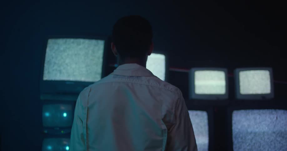 A man slowly backs up from the static filled television screens