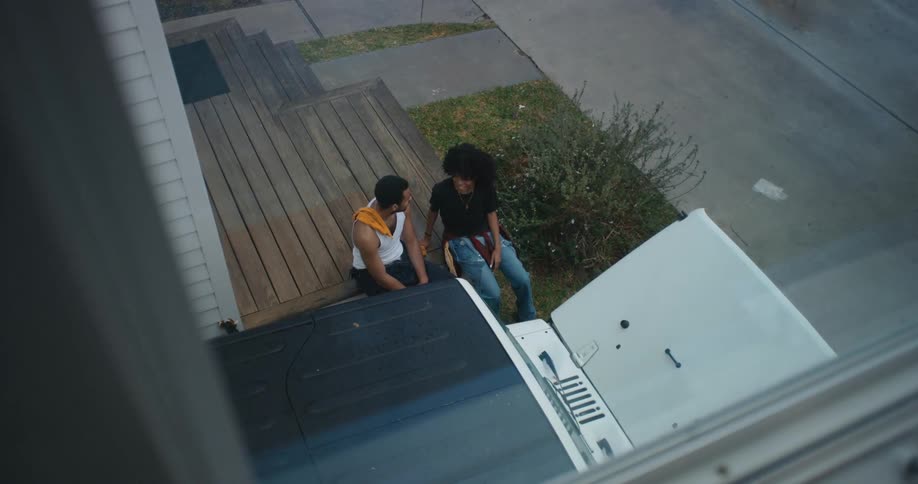 A man and woman talk with one another while sitting on the wooden porch of a house