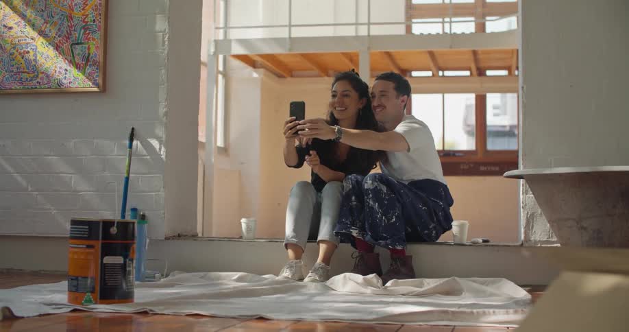 Smiling paint splattered couple pans mobile phone around room to show freshly painted walls