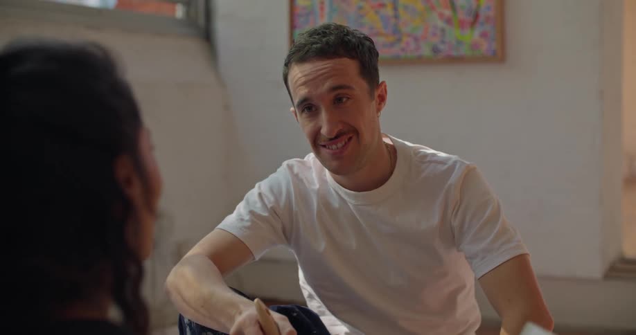 Man moves brush through large paint can as he and woman discuss paint sample cards