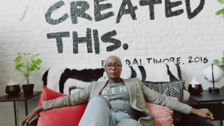 Woman sits on couch wearing fashionable clothes in front of a wall that makes a statement