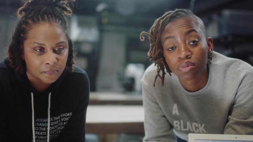 Two teenage girls lean over a display of laptops as they listen to an employee