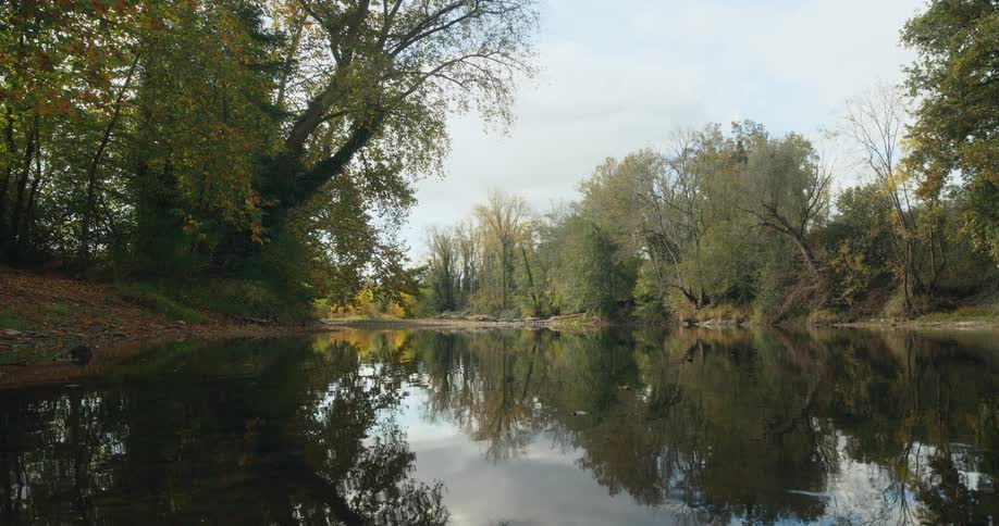 Slightly rippling water reflects the sky and the trees on shore