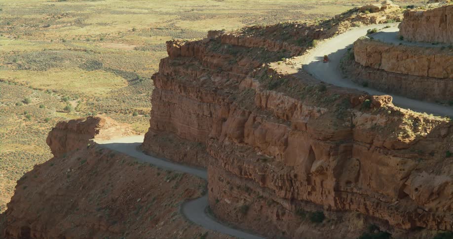 A vehicle travels along a winding road on a butte in the countryside during the day