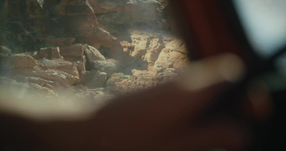 The surrounding rock canyon and desert are reflected in the side mirror and seen through the window of a car being driven