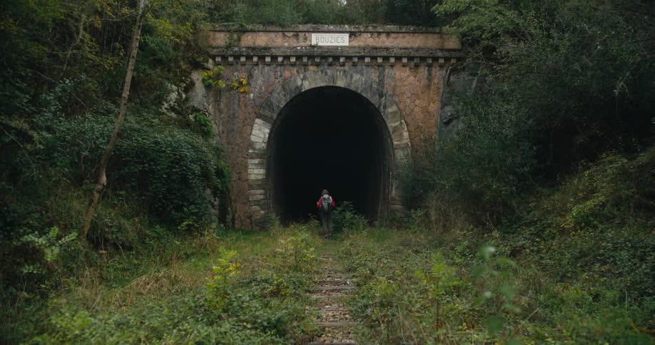 A hiker stands outside of an abandoned tunnel in a woodland for a moment before beginning to walk inside