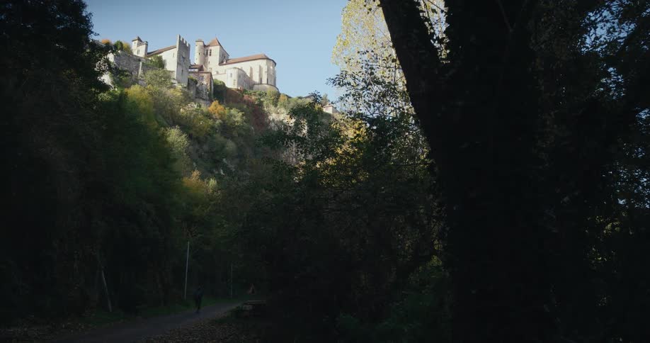 A hiker walks along a pathway through a woodland beneath a cliff during the day