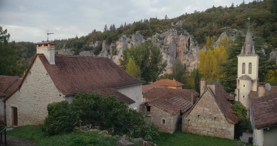 The stone homes and church of a french village in a valley with cliffs behind